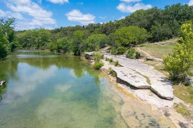 Clear green water on the Blanco River beside a limestone bank
